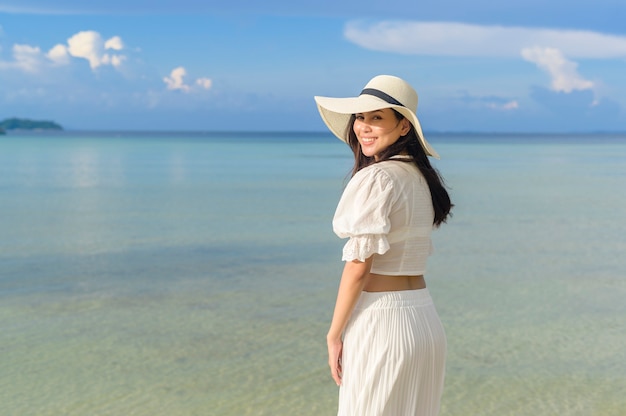 Una mujer hermosa feliz en vestido blanco disfrutando y relajándose en la playa, el concepto de verano y vacaciones