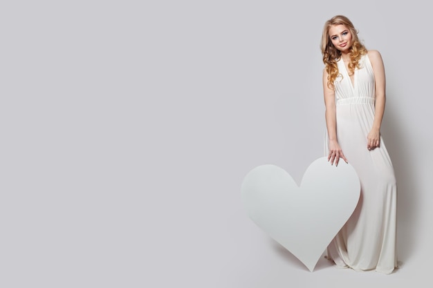 Mujer hermosa con fondo de corazón blanco Modelo bonito en perfecto vestido blanco