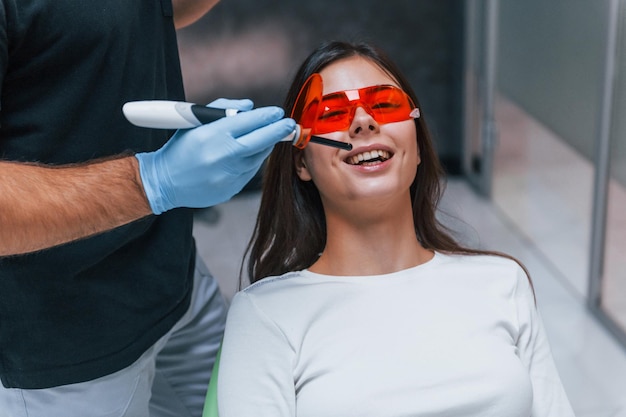 Una mujer hermosa con gafas protectoras rojas tiene una visita en la clínica del dentista. Concepción de la estomatología.