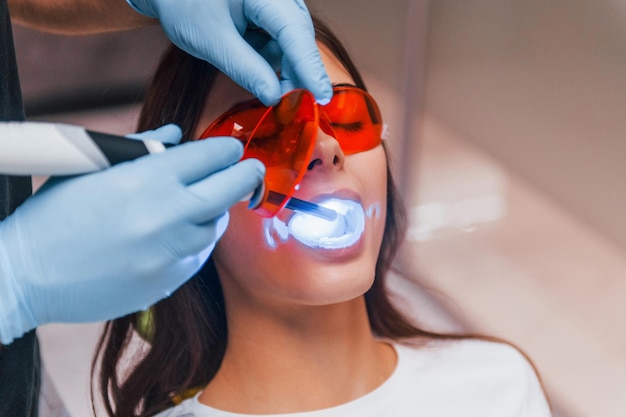 Una mujer hermosa con gafas protectoras rojas tiene una visita en la clínica del dentista. Concepción de la estomatología.