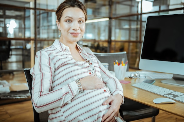 Mujer hermosa. Hermosa mujer embarazada con elegante blusa y accesorios tocando su barriga