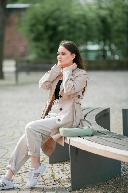 Mujer hermosa joven de 19 años con ropa elegante Modelo con cabello oscuro con ropa informal camina por la ciudad floreciente de primavera Cálida