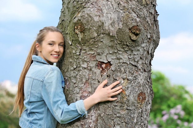 Mujer hermosa joven abrazando tronco de árbol