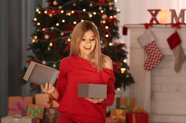 Mujer hermosa joven abriendo la caja de regalo en la habitación decorada para Navidad