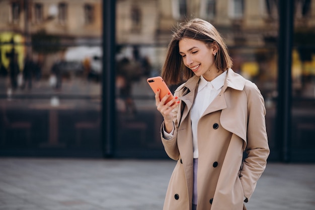 Mujer hermosa joven con abrigo caminando en la ciudad y hablando por teléfono