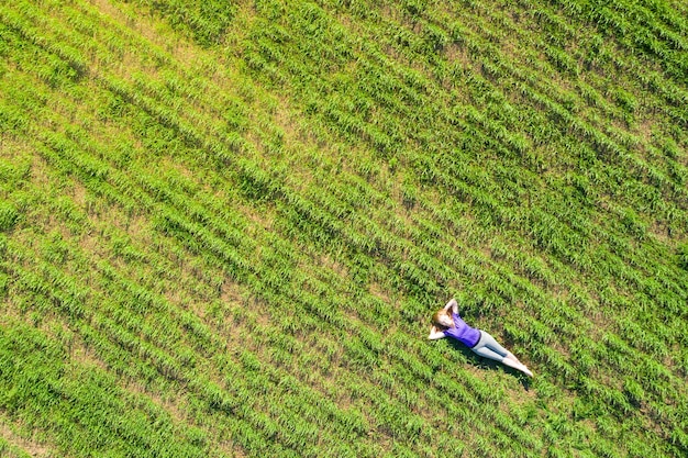 Mujer hermosa joven se acuesta y se relaja en la pradera verde en un día soleado. Vista aérea.