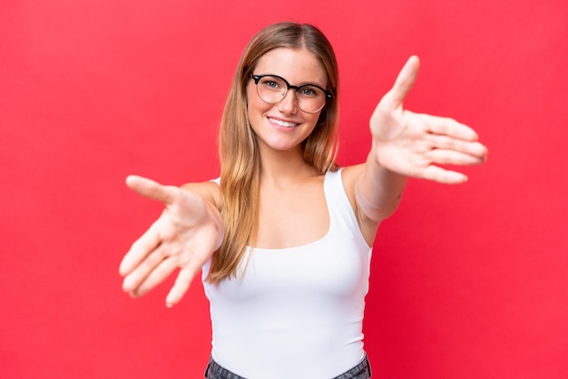 Mujer hermosa joven aislada de fondo rojo que presenta e invita a venir con la mano