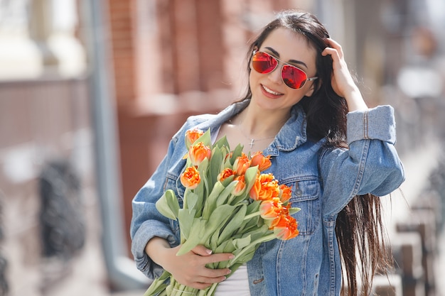 Mujer hermosa joven al aire libre en primavera. Chica atractiva cerca retrato. Señora con regalos, presenta cajas. Mujer con flores. Mujer alegre celebración de tulipanes.