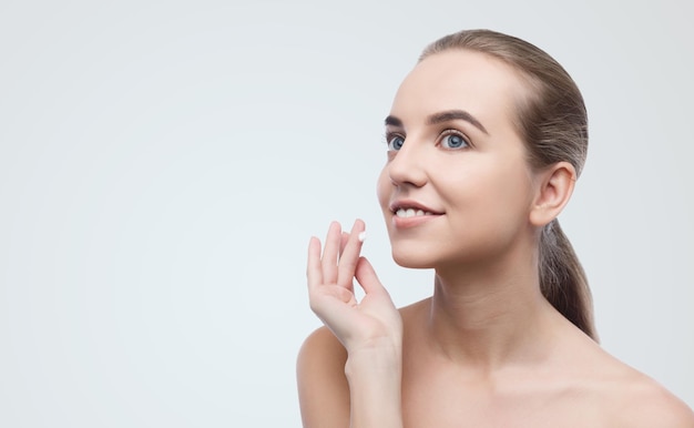 Mujer hermosa joven aplicando crema facial sobre fondo gris