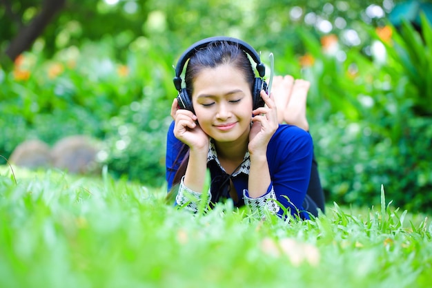 Mujer hermosa joven asiática se encuentran en la hierba para escuchar música