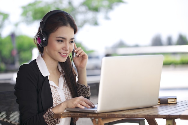 Mujer hermosa joven asiática que trabaja en la computadora portátil en la cafetería