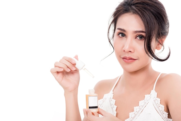 Mujer hermosa joven asiática sonriendo que sostiene una botella de suero para el cabello o el cuidado de la piel