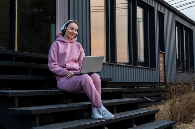 Mujer hermosa joven en auriculares con una computadora portátil está sentada en los escalones al aire libre dedicada a freela