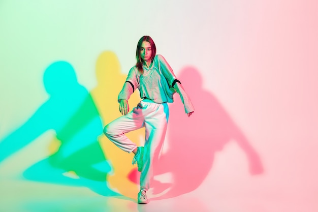 Mujer hermosa joven bailando hip-hop, estilo callejero aislado sobre fondo de estudio en luz de neón