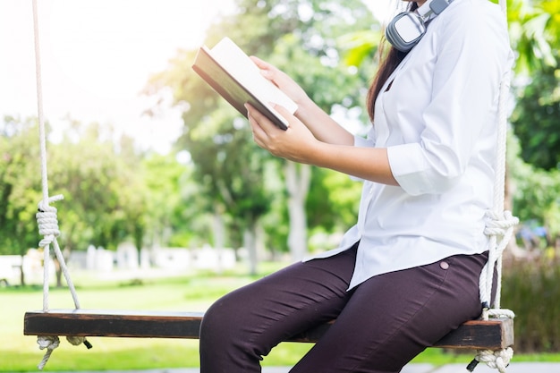 Mujer hermosa joven bastante relajada que lee un libro en el césped del jardín con el sol que brilla.