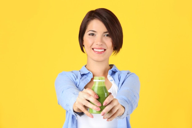 Mujer hermosa joven con batido verde sobre fondo amarillo