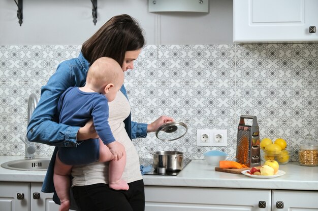 Mujer hermosa joven con bebé en brazos en la cocina