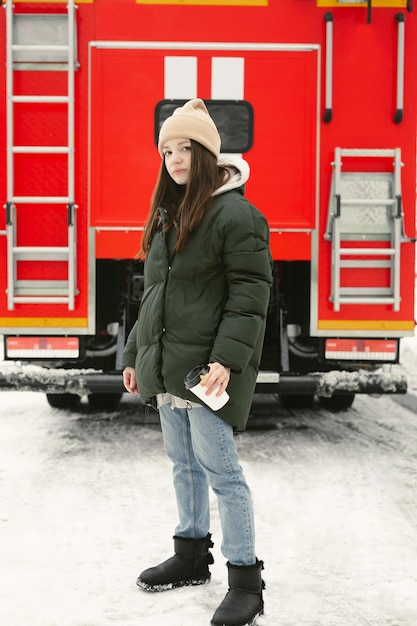 Mujer hermosa joven bebe café en invierno en una calle de la ciudad con un camión de bomberos rojo