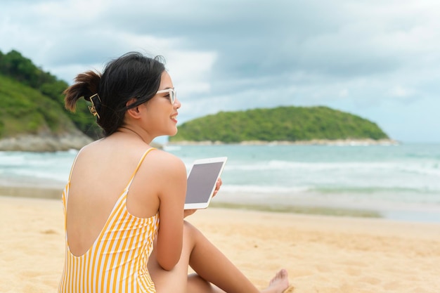 Mujer hermosa joven en Bikini relajándose y usando tableta en la playa