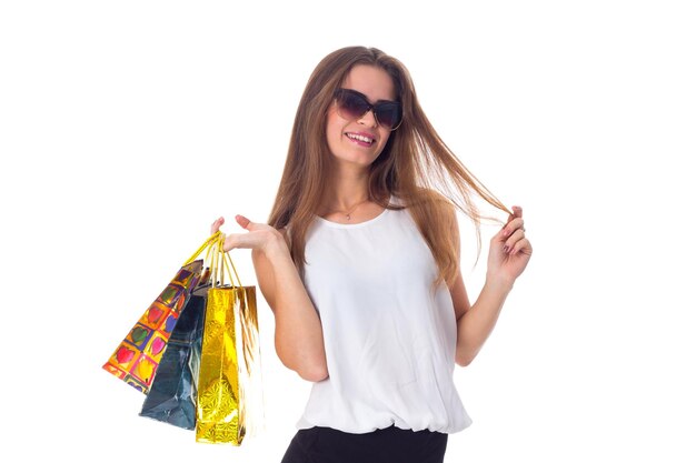 Mujer hermosa joven en blusa blanca y falda negra con gafas de sol oscuras sosteniendo bolsas de compras