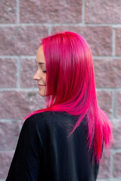 Mujer hermosa joven con cabello rosado sobre fondo de pared de ladrillo