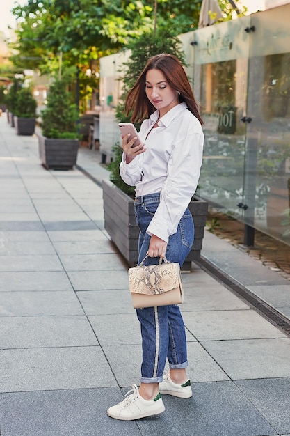 Mujer hermosa joven camina en la ciudad Retrato de niña en la calle manos con teléfono Aprendizaje a distancia de trabajo en línea