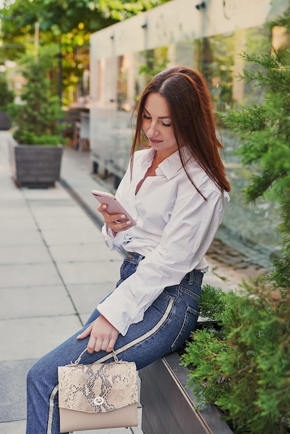 Mujer hermosa joven camina en la ciudad Retrato de niña en la calle manos con teléfono Aprendizaje a distancia de trabajo en línea