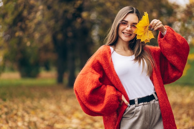 Mujer hermosa joven caminando en el parque de otoño y sosteniendo hojas