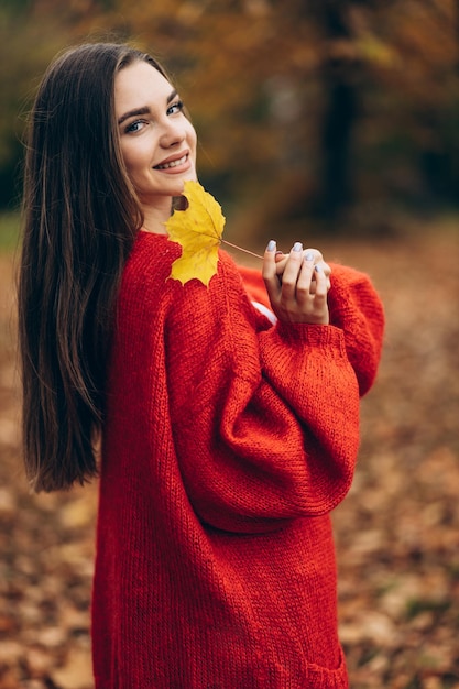 Mujer hermosa joven caminando en el parque de otoño y sosteniendo hojas