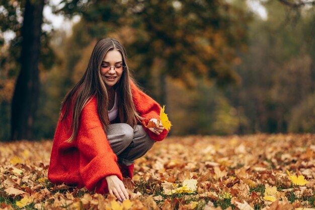 Mujer hermosa joven caminando en el parque de otoño y sosteniendo hojas