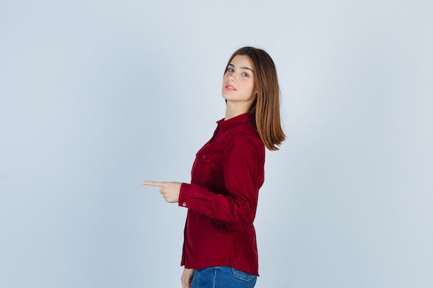 Mujer hermosa joven en camisa apuntando a la izquierda y mirando alegre