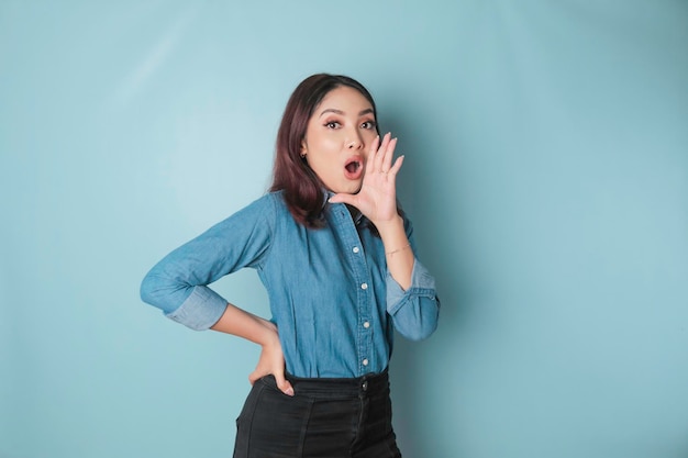 Mujer hermosa joven con una camisa azul gritando y gritando fuerte a un lado con una mano en la boca concepto de comunicación