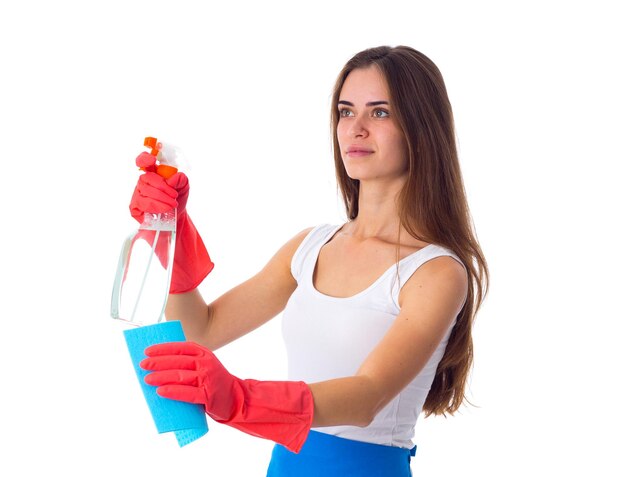 Mujer hermosa joven en camisa blanca y delantal azul con guantes rojos con plumero y detergente