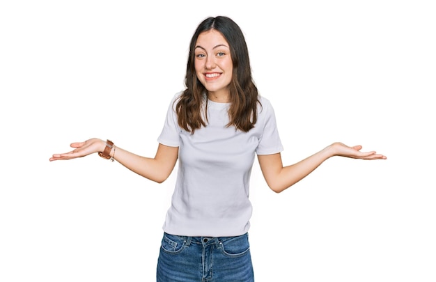 Mujer hermosa joven con camiseta blanca casual sonriendo mostrando ambas manos palmas abiertas presentando y publicitando comparación y equilibrio