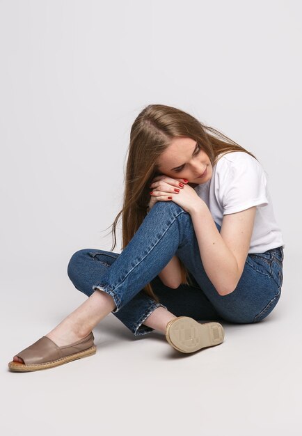 mujer hermosa joven en una camiseta blanca y pantalones vaqueros sobre un fondo blanco. Mujer joven sentada en blanco