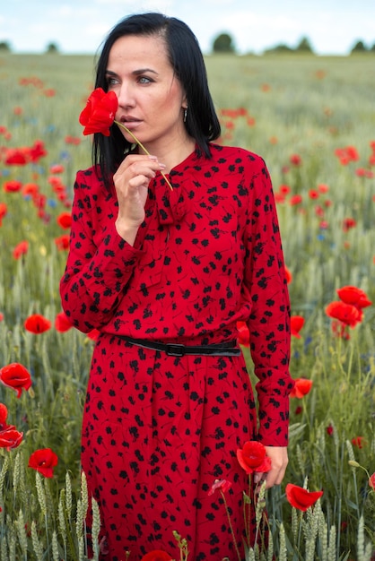 Mujer hermosa joven en el campo de amapolas de flores de verano