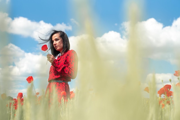 Mujer hermosa joven en el campo de amapolas de flores de verano