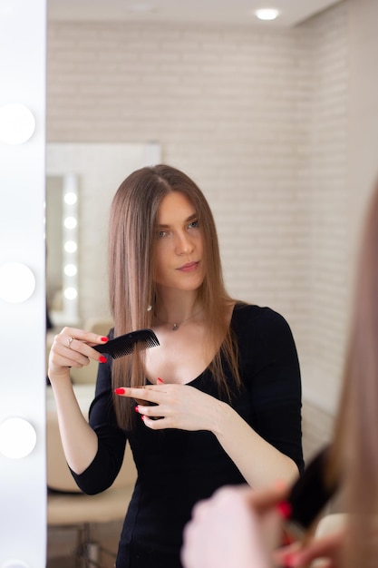 Mujer hermosa joven cepillando su cabello largo y saludable morena y mirando en el espejo