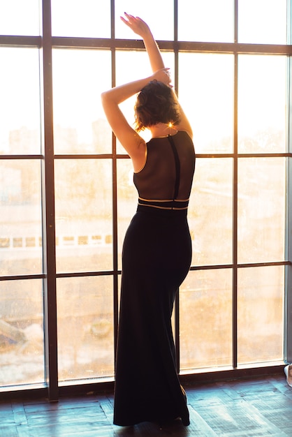 Mujer hermosa joven cerca de una ventana grande al atardecer