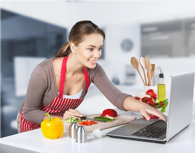 Mujer hermosa joven cocinando en la cocina con el portátil