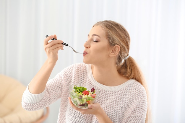 Mujer hermosa joven comiendo ensalada fresca en casa