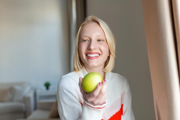 Mujer hermosa joven comiendo manzana fresca y mirando por la ventana