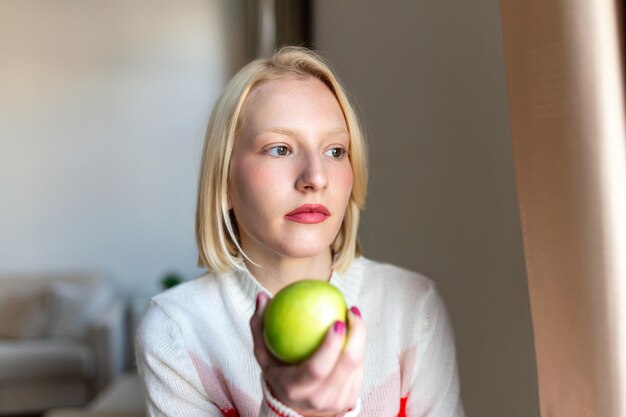 Mujer hermosa joven comiendo manzana fresca y mirando por la ventana