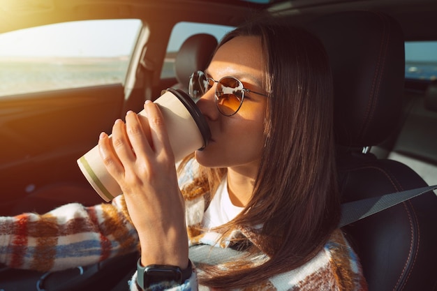 Mujer hermosa joven conduciendo un coche y bebiendo café