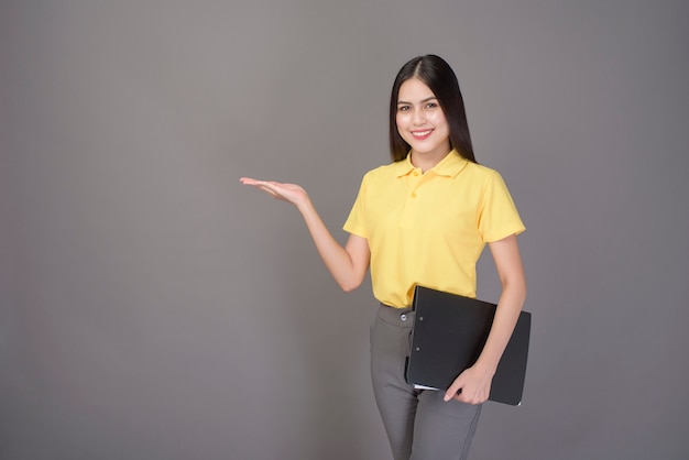 La mujer hermosa joven confiada que lleva la camisa amarilla está sosteniendo documentos en gris