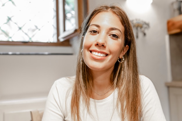 Mujer hermosa joven confiada que sonríe mirando a la cámara para una conferencia de video llamada en su casa