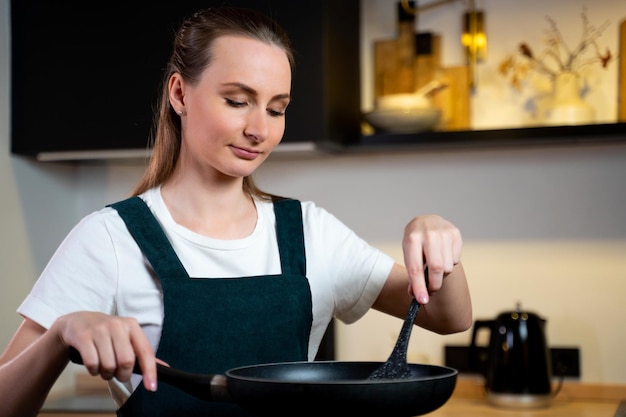 Una mujer hermosa joven disfruta cocinando comida saludable en una sartén en la cocina en casa feliz wom