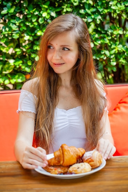 Mujer hermosa joven disfrutar del desayuno comer panadería fresca en el restaurante al aire libre