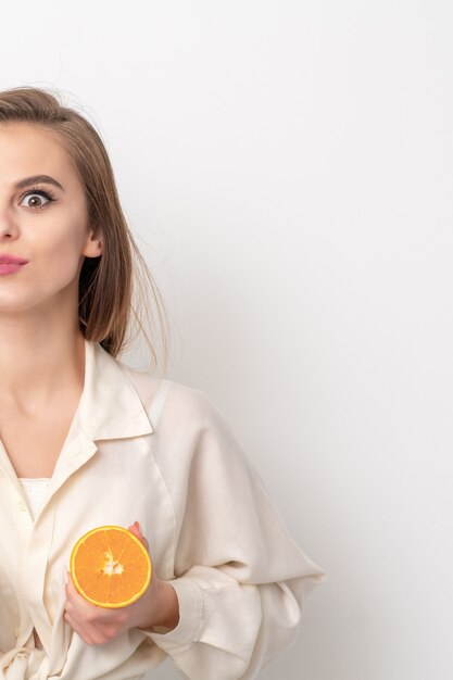 Mujer hermosa joven con dos piezas de naranja sobre fondo blanco.