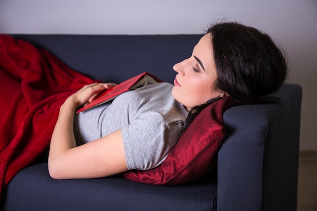 Mujer hermosa joven durmiendo con un libro en el sofá en casa